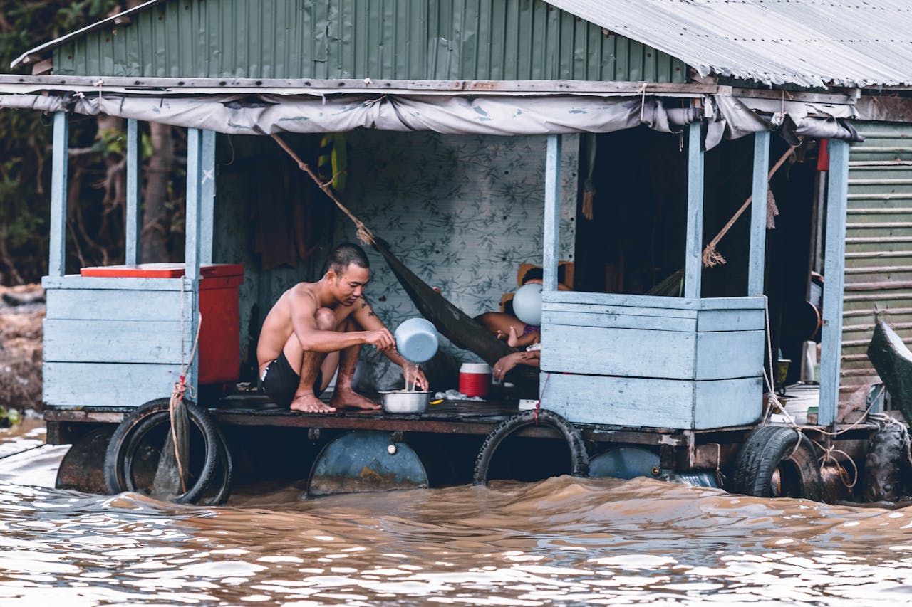 A man sits on a flooded wooden houseboat during a heavy flood.